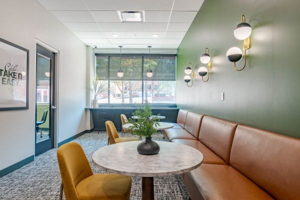 A bright and modern study lounge with large windows, orange chairs, and cozy seating at Chronicle on 8th.