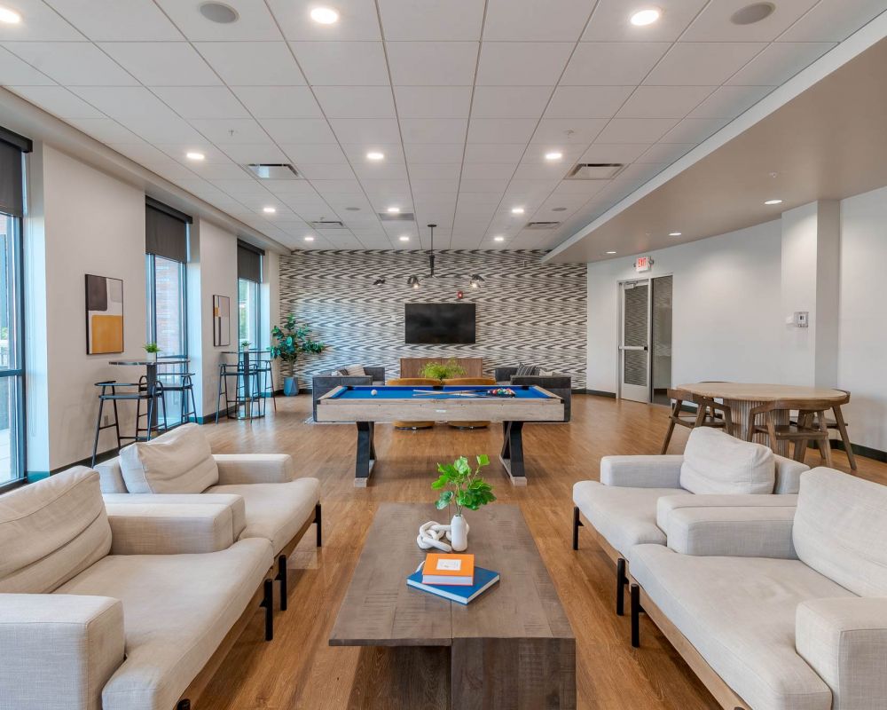 A modern game room featuring a pool table, comfortable lounge seating, and a wall-mounted TV, offering residents a stylish space to relax and connect at District Flats Columbia.