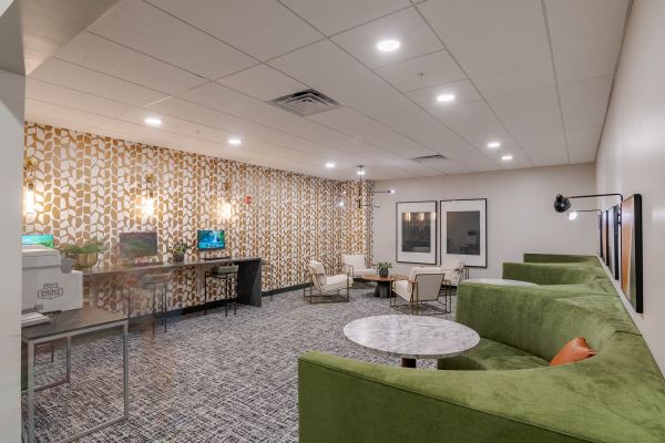Modern lounge with green sectional sofa, marble tables, armchairs, and patterned wallpaper.
