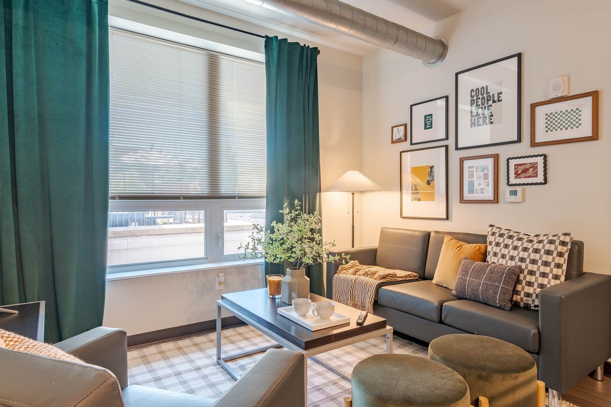 Stylish living room at Chronicle on 8th featuring a gray sectional sofa, framed wall art, large windows with teal curtains, and modern decor accents.