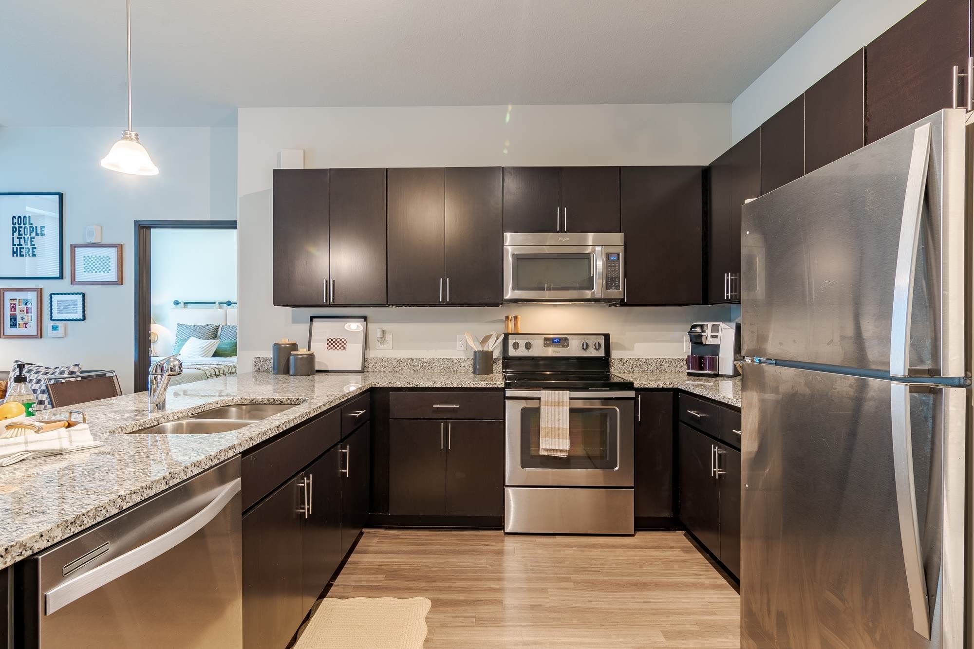 Contemporary kitchen at Chronicle on 8th featuring stainless steel appliances, dark wood cabinetry, light countertops, and hardwood-style flooring.